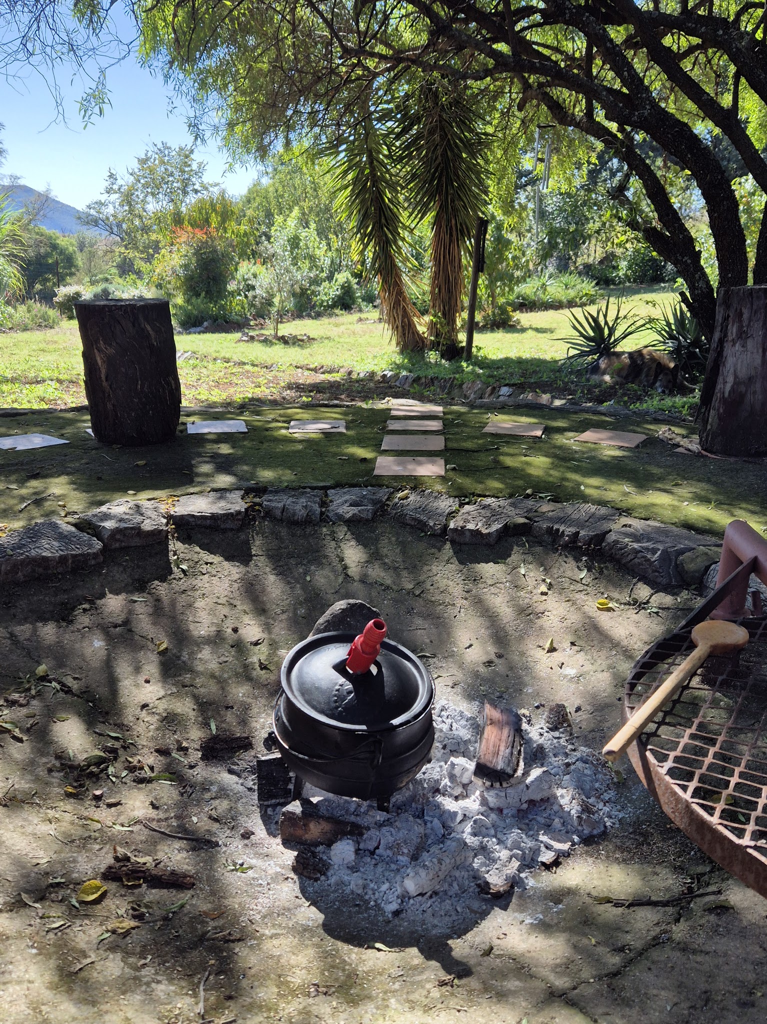 Braai-Platz mit Potjie-Topf am Feuer, umgeben von Garten und Bäumen